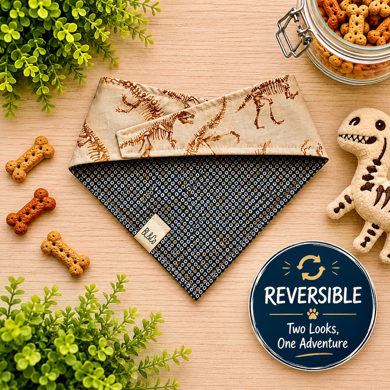 Reversible dog bandana with dinosaur pattern on a wooden surface with pet treats and toy.